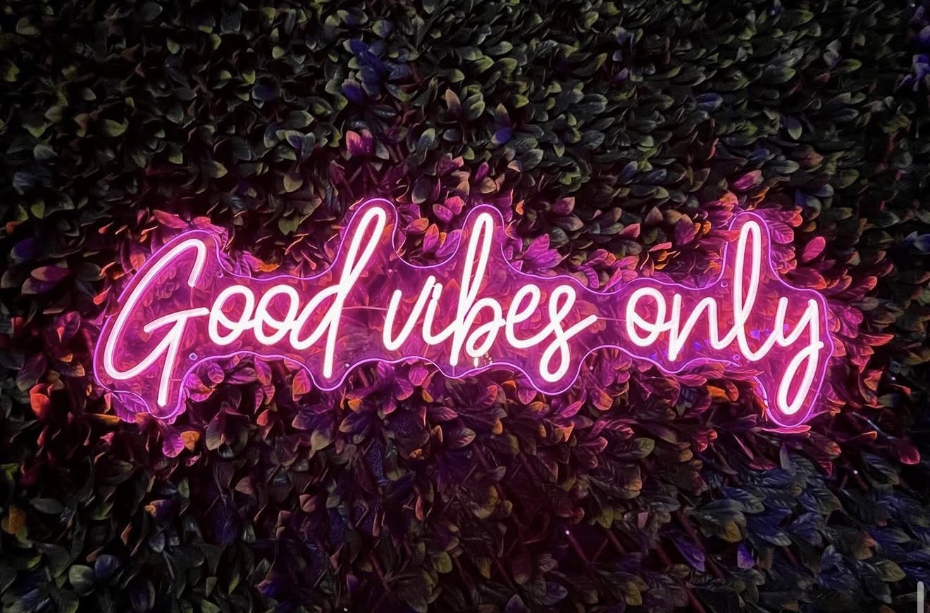 Good Vibes Only — néon rose sur mur végétal